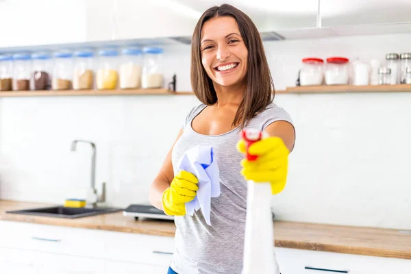 Decidida esposa en guantes amarillos está lista para empezar a limpiar su cocina moderna y se burla de dirigir el aerosol a la cámara, sonriendo . — Foto de Stock