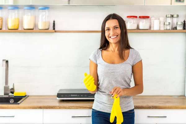 Dona de casa colocando luvas amarelas para lavar pratos na cozinha . — Fotografia de Stock