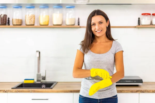 Dona de casa colocando luvas amarelas para lavar pratos na cozinha . — Fotografia de Stock