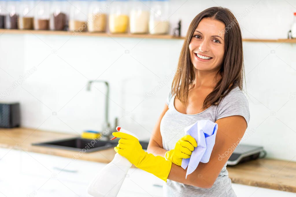 Charming female in protective gloves with spray and cloth to clean her kitchen.