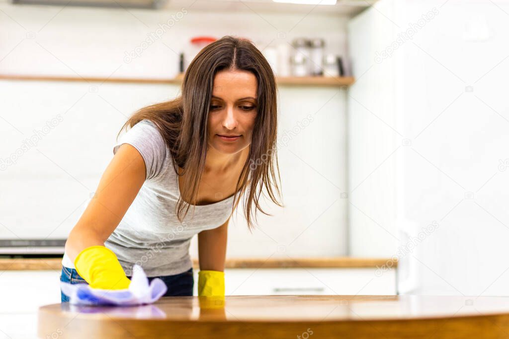 Charming female in protective gloves cleaning kitchen using spray and cloth.