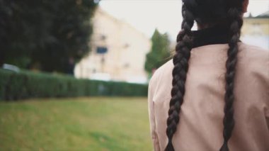 Yavaş ol. Uzun siyah örgülü sevimli ve genç bir turist gülümsüyor ve kameraya doğru dönüyor. Kapatın. Uzayı kopyala 4K.