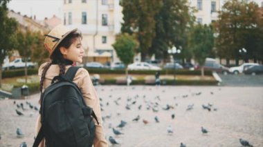 Yavaş ol. Uzun siyah örgüleri ve şapkası olan sevimli ve genç bir turist gülümsüyor ve kameraya doğru dönüyor. Kapatın. Uzayı kopyala 4K.