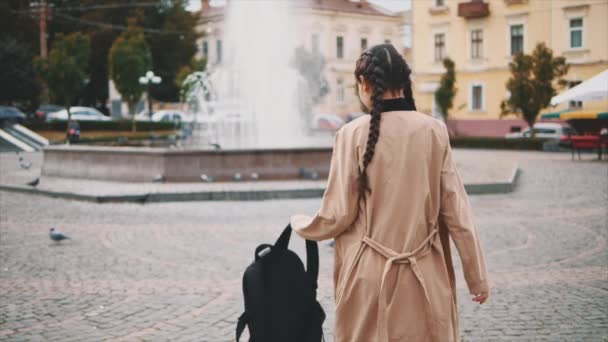 Menina adorável vira e segurando mochila turística preta na praça, cheia de pombos. Movimento lento. Espaço para cópia. 4K . — Vídeo de Stock