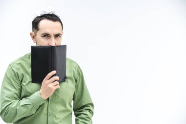 Olgun iş adamı, beyaz arkaplan üzerinde şüpheli, güvenilmez yüz ifadesi olan, metin veya ürün için telif alanı olan siyah defterin üzerinden gözetliyor..