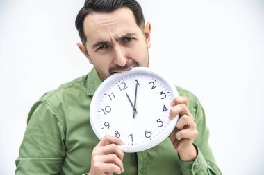 Tamamen yorgun bir adam beyaz bir arka planda çalar saati ısırıyor..