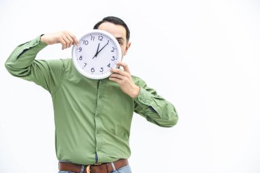Yeşilli genç adam bekliyor, beyaz arka plan üzerinde saati gözünün önünde tutuyor..