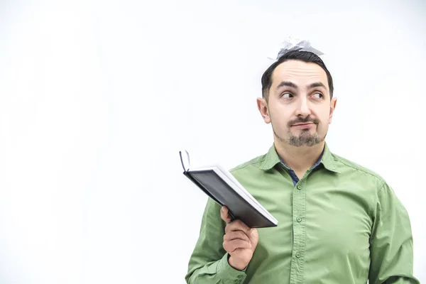 Young foolish man with crumpled paper on his head and opened organizer in hands over white background. — Stock Photo, Image