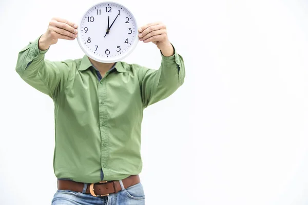 Young man in green is waiting, holding clock in front of his face over white background. — Stock Photo, Image