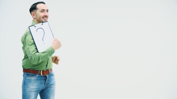 Joven divertido bailando con la celebración de un titular de papel con escrito en él signo de interrogación, mirando sorprendentemente a esta marca y señalando con el dedo . — Vídeos de Stock