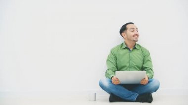 Loto pozisyonunda dizlerinin üzerinde dizüstü bilgisayarı ve yanında beyaz bir bardakla oturmuş ne kadar güçlü olduğunu gösteren bir gülümsemeyle kendini yalnız hisseden genç bir adam..