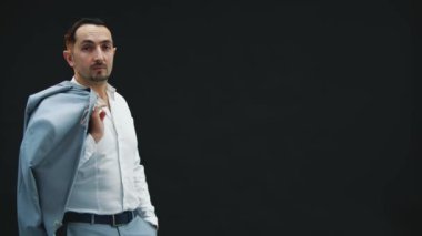 Yakışıklı genç adam siyah arkaplanda beliriyor omzunda ceketle, kameraya anlamlı bir şekilde bakıyor, WTW işareti gösteriyor.