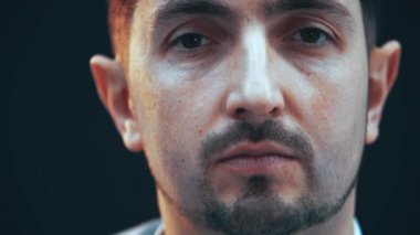 Ciddi genç konsantre bir adam kameraya bakıyor, sonra gözlerini kapıyor..