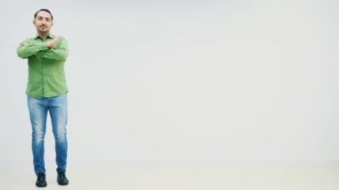 Uzun boylu, yakışıklı, sıradan bir adam beyaz arka planda beliriyor, ellerini katlıyor, yana bakıyor, ayağını yere vuruyor. Komik yüz ifadesi.