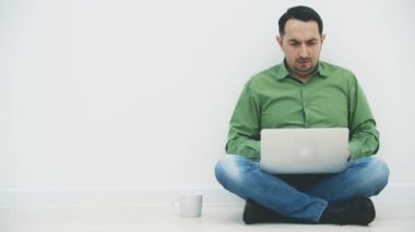 Loto pozisyonunda dizüstü bilgisayarla oturan, internette arama yapan, sert kahve içen ciddi bir genç adam..