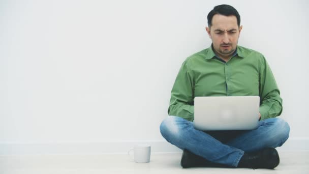 Bostezar joven serio sentado en la posición lotos con el ordenador portátil, la búsqueda en Internet, beber café fuerte . — Vídeos de Stock