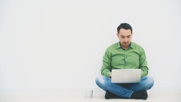 Ung man sitter på golvet i lotos position med laptop, söker på internet, hitta något trevligt, höjer glatt händerna upp, kysser laptop, visar sin makt. — Stockvideo