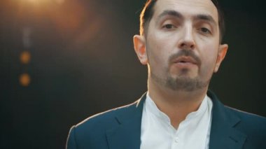 Ciddi bir genç adam kameraya bakıyor, kıyafetlerini düzeltiyor ve eğiliyor..