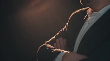 Elleri katlanmış, gergin bir şekilde ayağını yere vuran yakışıklı bir adam..