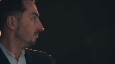 Ciddi genç yakışıklı adam ayakta duruyor, kameraya bakıyor, sonra yana bakıyor, biriyle konuşuyor..