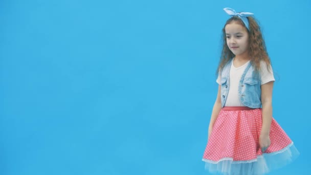 LIttle menina de pé sobre fundo azul em 4k slow motion vídeo. — Vídeo de Stock