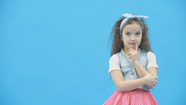 Malá dívka rozhodování nad modrým pozadím v 4k zpomalení videa. — Stock video