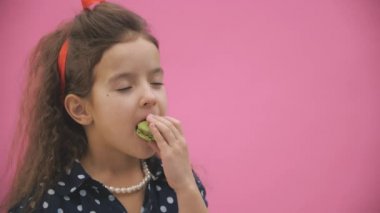 Kıvırcık saçlı küçük bir kızın yeşil bir badem kurabiyesi yediği 4K yavaş çekim videosu..