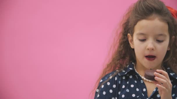 Niña sobre fondo rosa comiendo un macarrón marrón en 4k slow motion video . — Vídeo de stock