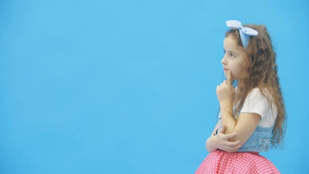 Küçük kız 4K videosunda mavi arkaplan üzerinde karar veriyor. — Stok video