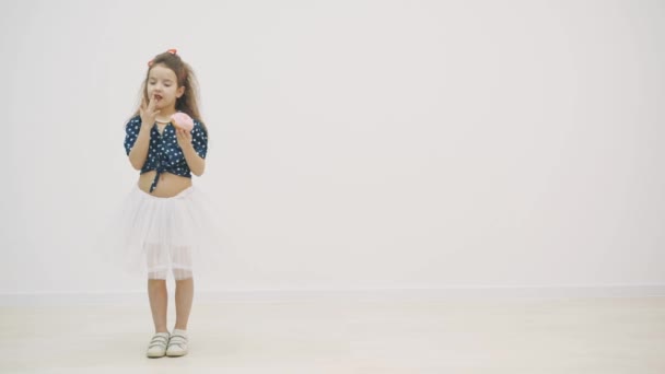 4k video donde la niña lamiéndose los dedos después de sostener una rosquilla acristalada dulce en las manos . — Vídeo de stock