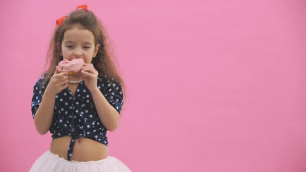 폴카 점을 입은 어린 소녀는 4k 비디오에서 맛있는 도넛을 먹는다. — 비디오
