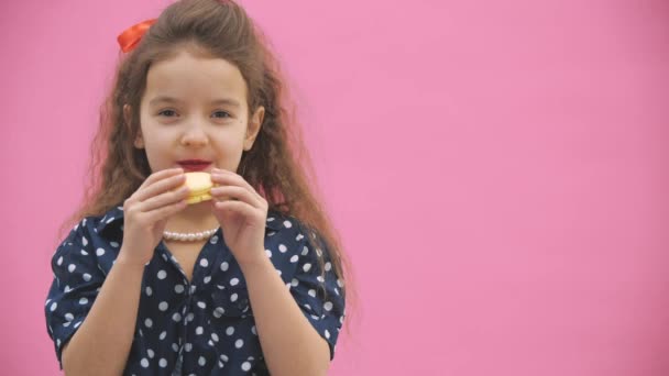 4k 클로즈업 비디오는 곱슬머리의 작은 소녀가 노란색 마카롱을 먹는 모습을 담고 있다. — 비디오