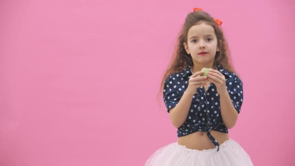 4k video donde niña con el pelo rizado comiendo un macarrón verde . — Vídeos de Stock