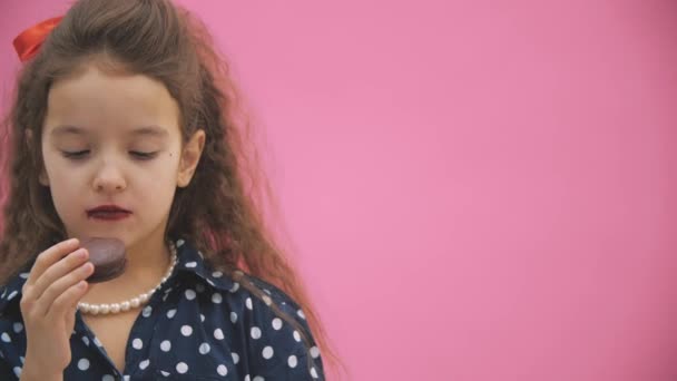 핑크 색 배경의 여자 아이가 4k 비디오에서 갈색 마카롱을 먹고 있습니다.. — 비디오