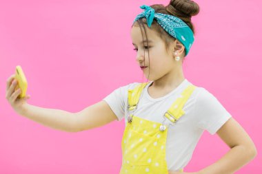 Küçük kız selfie çekiyor ve pembe arka planın önünde duruyor..