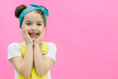 Küçük kız yanaklarına dokunuyor ve gülümsüyor.