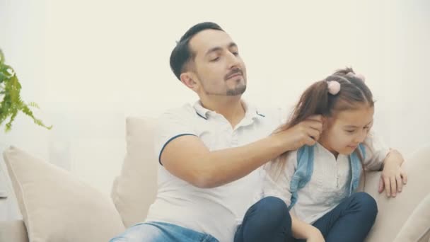 4k wideo z widokiem, gdzie tata dotyka jego córka włosy na białej kanapie w salonie. — Wideo stockowe