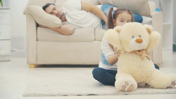 4k video waar dochter met witte teddybeer in de buurt van zijn ontspannen vader. — Stockvideo