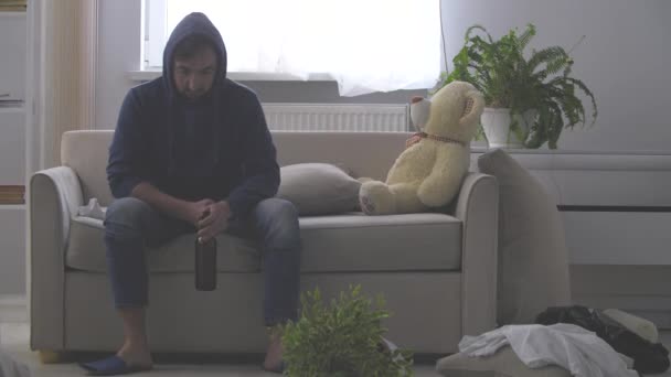 4k video donde el hombre sentado en el sofá mirando en el frente bebiendo su cerveza. — Vídeo de stock