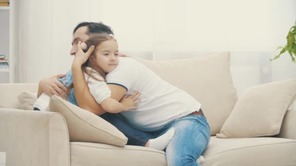 Vidéo de ralenti 4k où une petite famille s'étreint sur un canapé blanc . — Video