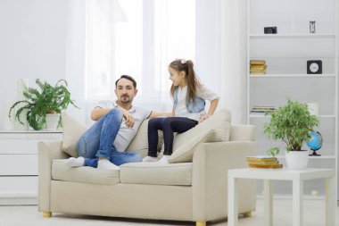 Baba ve kızı kanepede birlikte otururken eğleniyorlar..