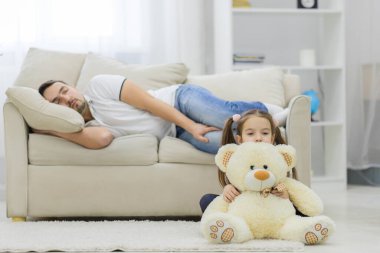 Babası uyuyor ve kızı beyaz ayıyla oturuyor..