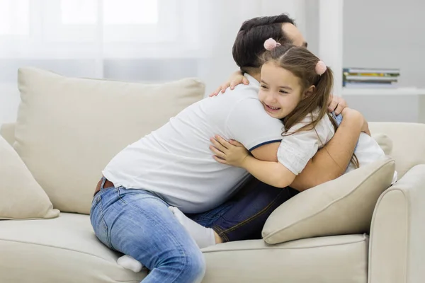 Father and daughter sitting on white sofa and hugging each other. — Stock Photo, Image