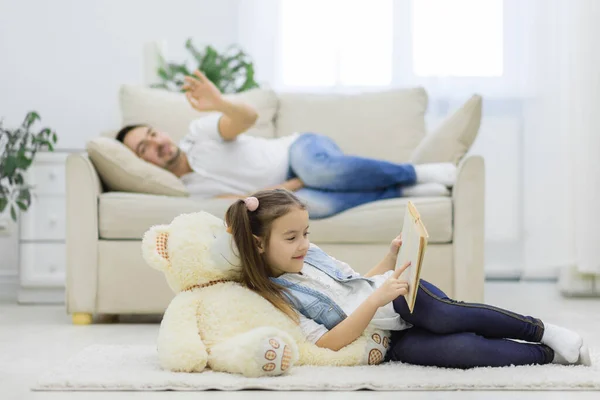 Vader is op de bank en kind lezen boek op de vloer. — Stockfoto