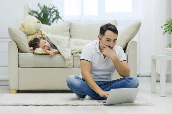 Papa ist online, während seine Tochter auf der Couch träumt. — Stockfoto
