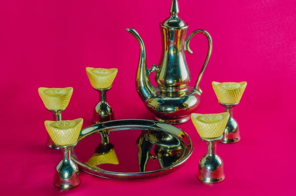 Lingote de oro jarra de oro vidrio de té placas de oro sobre fondo rojo . — Foto de Stock
