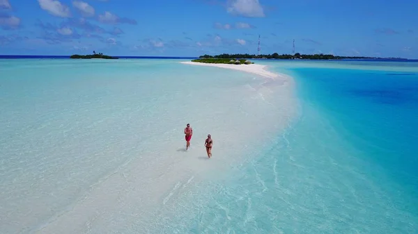 P02571 Aerial flying drone view of Maldives white sandy beach 2 people a young couple man woman walking on sunny tropical paradise island with aqua blue sky sea water ocean 4k