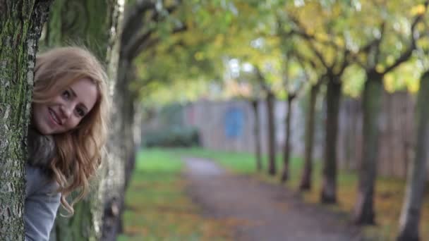 Joven mujer exhibida detrás de un árbol y sonriendo — Vídeos de Stock