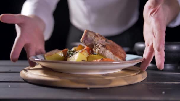 Cooks hand puts a fresh fried steak on white plate and maiking final decoration of dish. The cook sprinkles meat with salt, pepper, seasoning, spices and lemon juice. Serving food. — Stock Video