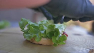 Yavaş hareket eden yiyecek konsepti. Şef hamburger yapıyor. Yakın plan. Burger restoranının menü pişirme işlemi. Şef restoranda fast food hazırlıyor. Siyah ekmeğe peynir sosu döküyor..